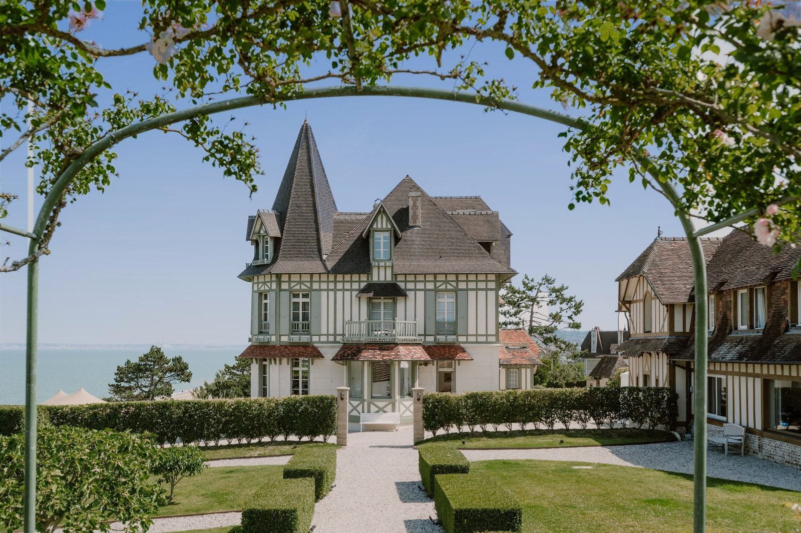 La maison de l'Abbaye vue depuis le jardin, à travers une arche fleurie